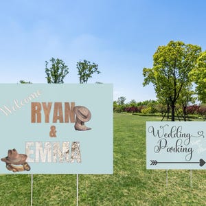 May include: Two light blue signs on metal stakes in a grassy field. One sign says "Welcome Ryan & Emma" with cowboy boots and hats. The other says "Wedding Parking" with an arrow.