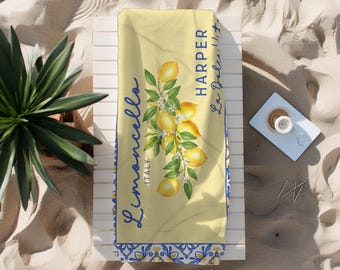 May include: Yellow beach towel with a lemon and floral design. The towel has the words "Limoncello Italy" and "Harper La Dolce Vita" in blue script. The towel is decorated with a blue and white border.