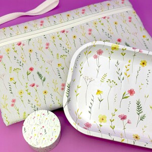 Peut inclure: Une pochette zipp&eacute;e en toile blanche avec un motif floral, un plateau en c&eacute;ramique blanche avec un motif floral et un petit r&eacute;cipient rond blanc avec un motif floral.
