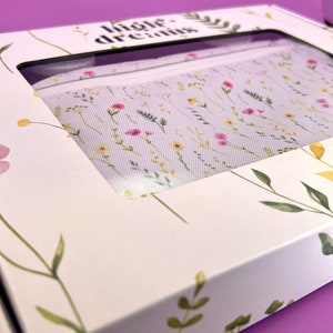 Peut inclure: Une bo&icirc;te blanche avec un motif floral et le texte "little dreams" imprim&eacute; sur le dessus. La bo&icirc;te est ouverte et une pochette en tissu blanc avec un motif floral est visible &agrave; l'int&eacute;rieur.