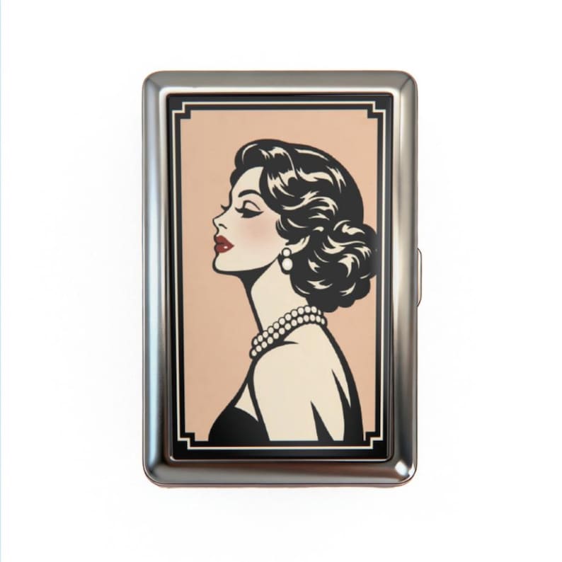 May include: A silver metal cigarette case featuring a retro illustration of a woman in profile. The woman has dark hair, red lipstick, and a pearl necklace. The background is a light peach color.