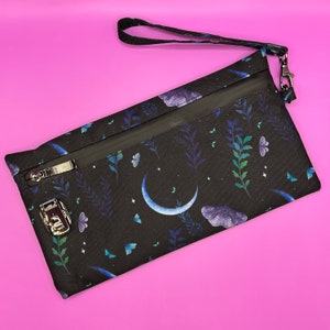 May include: A black zippered pouch with a moon and butterfly pattern. The pouch has a zipper closure and a silver lock. The pouch has a black strap.