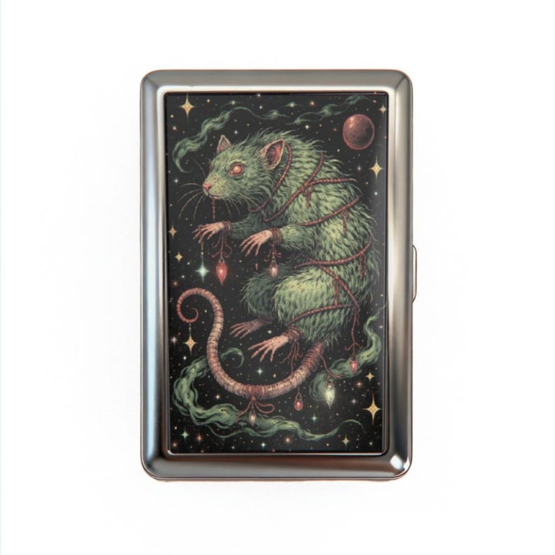 May include: A silver cigarette case featuring a green rat illustration against a starry night sky. The rat is wrapped in red rope and adorned with hanging jewels. The artwork has a fantasy theme.