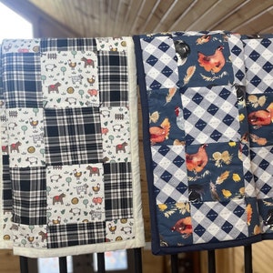 May include: Two patchwork quilts with a farm animal theme. One quilt is black and white plaid with a white background and features farm animals like cows, pigs, and chickens. The other quilt is blue and white with a diamond pattern and features chickens and feathers.