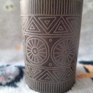 Może przedstawiać: Brązowy kubek ceramiczny z geometrycznym wzorem trójkątów i kół. Kubek ma fakturowaną powierzchnię.