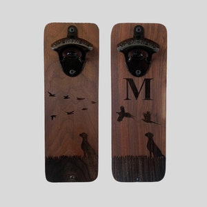 May include: Two wooden bottle openers with a black metal bottle opener. The left opener has a design of birds flying and a dog. The right opener has a design of a pheasant, a dog, and the letter M.