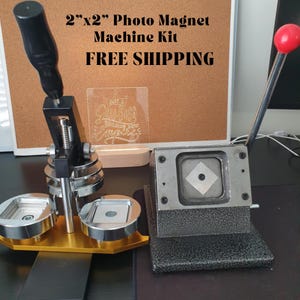 May include: A 2" x 2" photo magnet machine kit with a black handle, a silver press, and a grey base. The machine is used to create custom photo magnets. The kit includes two round moulds and a square mould. The machine is on a black surface. FREE SHIPPING.