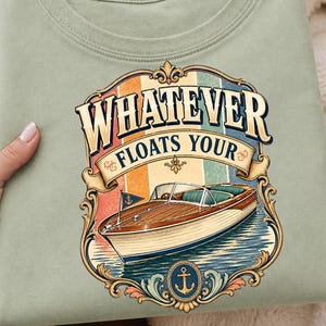 May include: A light green t-shirt featuring a vintage-style graphic. The graphic includes a wooden boat on water, with the text "WHATEVER FLOATS YOUR". The design is framed with decorative elements and an anchor.