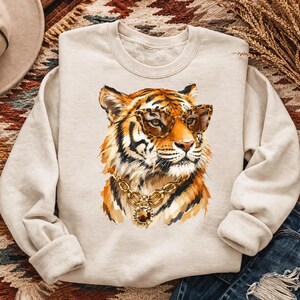 Könnte beinhalten: Beiges Sweatshirt mit einer Aquarellillustration eines Tigers mit Sonnenbrille und einer goldenen Halskette. Der Tiger hat orange und schwarze Streifen. Die Sonnenbrille hat ein Leopardenmuster.