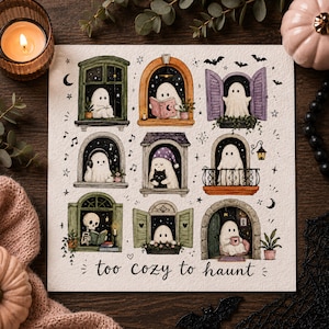 May include: A square art print featuring nine illustrations of ghosts in various windows, including one reading, one with a cat, and one with headphones. The text 'too cozy to haunt' is written in black cursive at the bottom of the white paper.