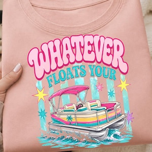May include: Pale pink t-shirt featuring a pontoon boat graphic and the text "WHATEVER FLOATS YOUR". The boat has a pink canopy, and blue, yellow, and white stripes, with stars and water around it.