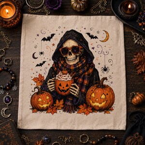 May include: A square beige fabric cloth featuring a central illustration of a skeleton wearing a dark hooded cloak, an orange and black plaid scarf, and orange-rimmed sunglasses. The skeleton holds a jack-o'-lantern mug filled with whipped cream.