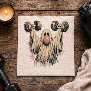 May include: A square paper napkin featuring a black and beige ink illustration of a ghost lifting two heavy dumbbells overhead. The ghost has a round pink bubblegum sphere in the center of its face and dark, hollow, oval-shaped eyes.
