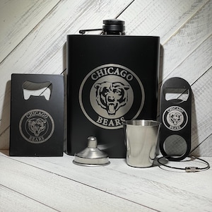 May include: A black flask with a Chicago Bears logo, a matching bottle opener, a shot glass, and a funnel. The flask, bottle opener, and shot glass all have the Chicago Bears logo.