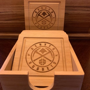 May include: Set of six wooden coasters with a Denver Nuggets logo engraved on each. The coasters are in a bamboo holder.