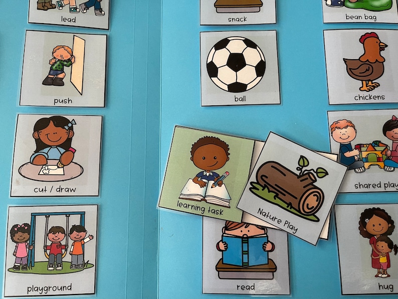 Op de afbeelding: Een verzameling ge&iuml;llustreerde kaarten met verschillende activiteitsprompts, waaronder "lead", "push", "cut/draw", "playground", "snack", "ball", "chickens", "learning task", "Nature Play", "read", "hug" en "shared play". De kaarten zijn gerangschikt op een lichtblauwe ondergrond.