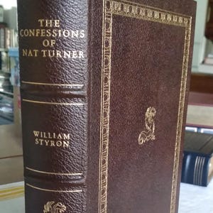 May include: A hardcover book titled "The Confessions of Nat Turner" by William Styron. The book has a brown leather cover with gold lettering and decorative accents. The Franklin Library imprint is visible.