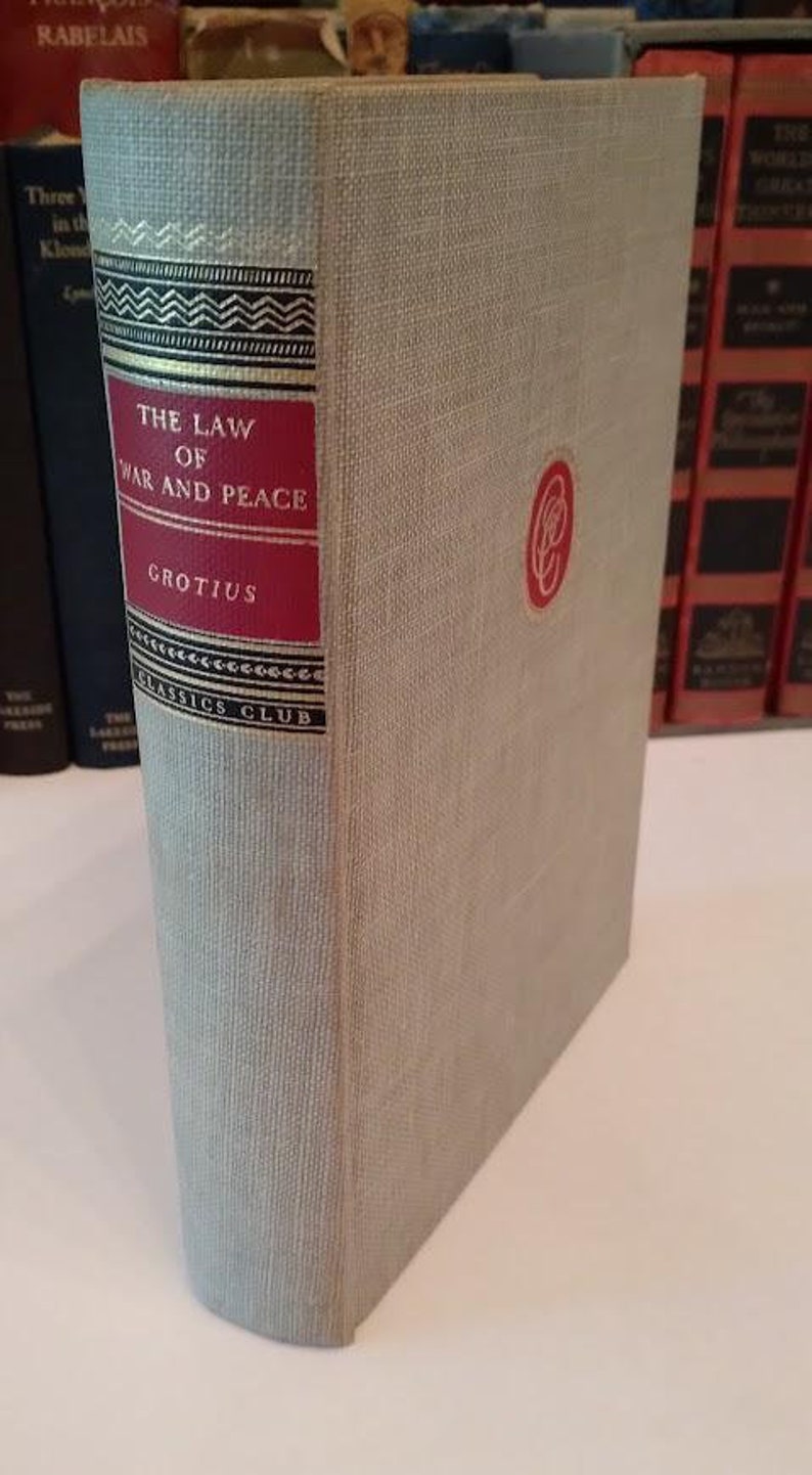 May include: A hardcover book titled "THE LAW OF WAR AND PEACE" by Grotius. The book has a light gray cover with a red label on the spine. The spine also features decorative black and gold accents and the Classics Club logo.