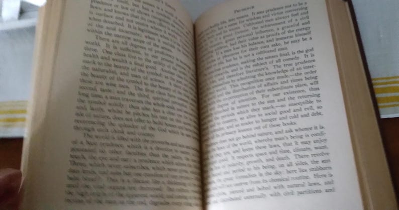 Pode incluir: Um livro aberto com p&aacute;ginas amareladas e envelhecidas. O texto &eacute; pequeno e denso, sugerindo uma obra cl&aacute;ssica ou vintage. A encaderna&ccedil;&atilde;o &eacute; vis&iacute;vel e o livro parece bem usado. As p&aacute;ginas est&atilde;o ligeiramente curvadas, indicando idade e uso.