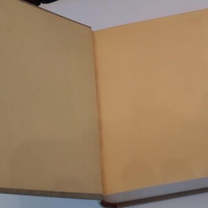 May include: An open book with tan-colored pages. The book is lying flat, revealing two facing pages. The edges of the pages are visible, and the book's spine is on the left side. The book appears to be old.