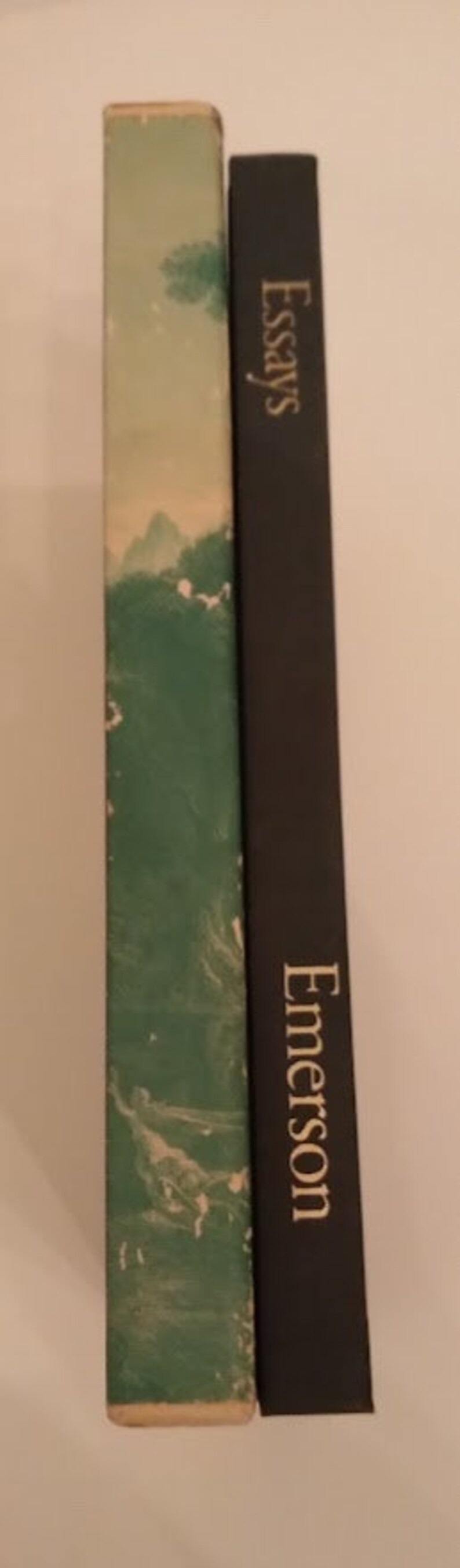 May include: Two hardcover books with green and black covers. The book on the left has a green cover with a swirling pattern and a white title. The book on the right has a black cover with the title "Essays" and the author's name "Emerson" in gold lettering.