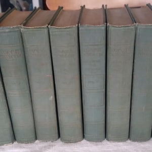May include: A collection of eight antique books with faded teal covers and brown spines. The titles are embossed in gold lettering. The books are arranged in a row, slightly angled, suggesting a vintage library or literary theme.