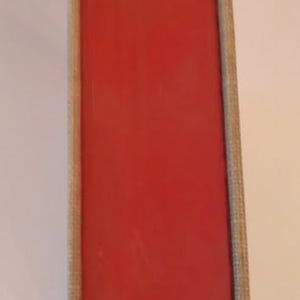 May include: A close-up of a book spine with a vibrant red cover. The edges are a light beige color, and the book is part of a collection. The spine is smooth and appears to be in good condition.