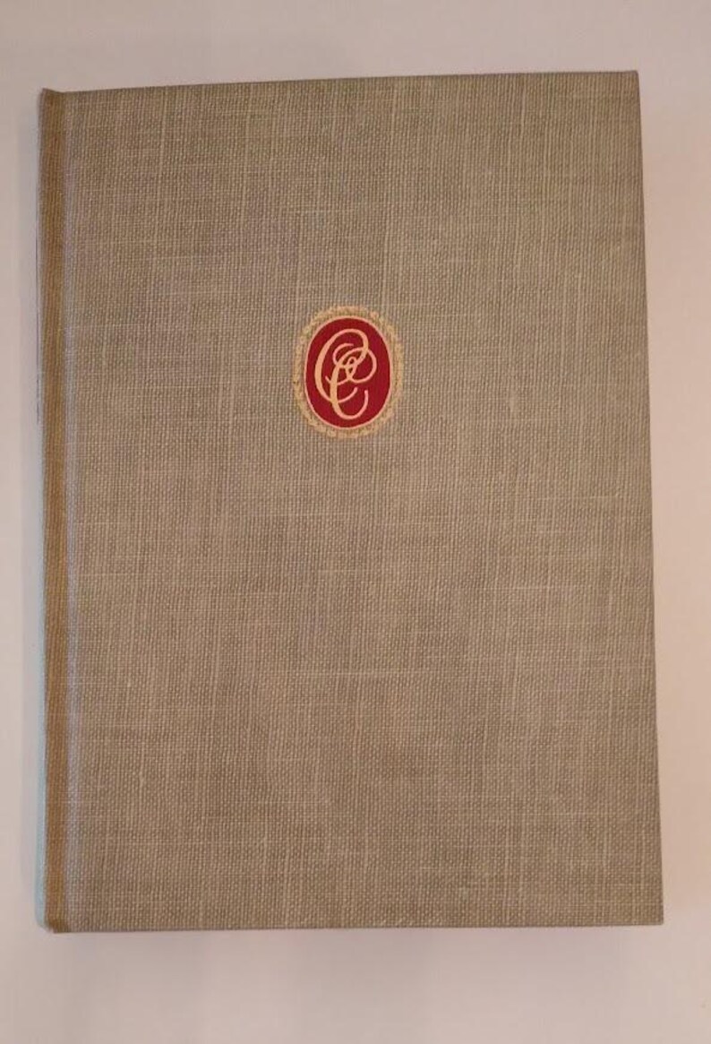 May include: A beige linen-textured book with a red and gold emblem on the cover. The book has a simple, classic design, with a slightly rounded spine. The cover is a solid, neutral color.