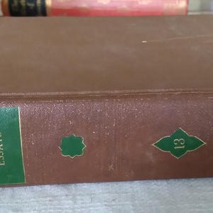Pode incluir: Um livro de capa dura castanho com os t&iacute;tulos "World's Greatest Literature" e "Emerson's Essays" na lombada. A lombada apresenta etiquetas verdes com texto dourado e formas verdes decorativas. O n&uacute;mero "13" tamb&eacute;m &eacute; vis&iacute;vel.