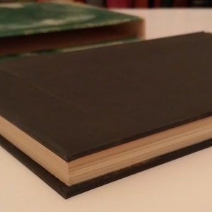 May include: A dark green hardcover book with a light brown spine. The book is closed and lying on a white surface.