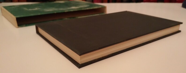 May include: A dark green hardcover book with a light brown spine. The book is closed and lying on a white surface.