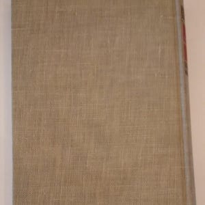 May include: A hardcover book with a beige linen cover. The spine is visible on the right side, with a light blue edge and some red text. The cover has a textured appearance.