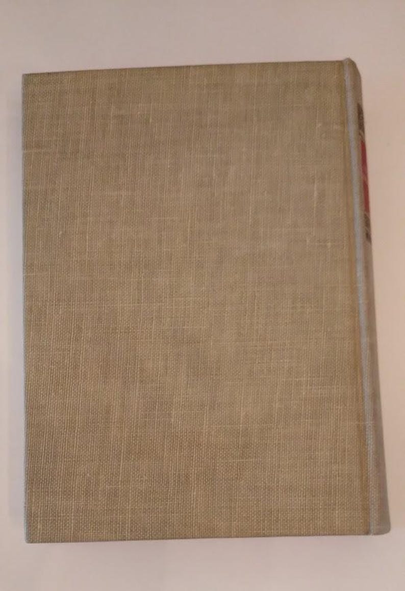 May include: A hardcover book with a beige linen cover. The spine is visible on the right side, with a light blue edge and some red text. The cover has a textured appearance.
