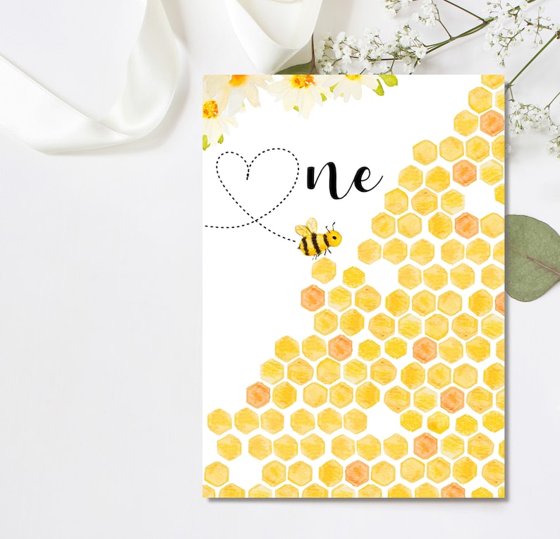 Puede incluir: Una tarjeta blanca con un patr&oacute;n de panal amarillo y una abeja volando hacia la palabra "uno" con un coraz&oacute;n encima.
