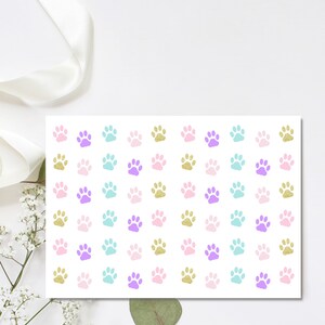 May include: A sheet of white paper with a repeating pattern of paw prints in pink, purple, turquoise, and gold glitter.