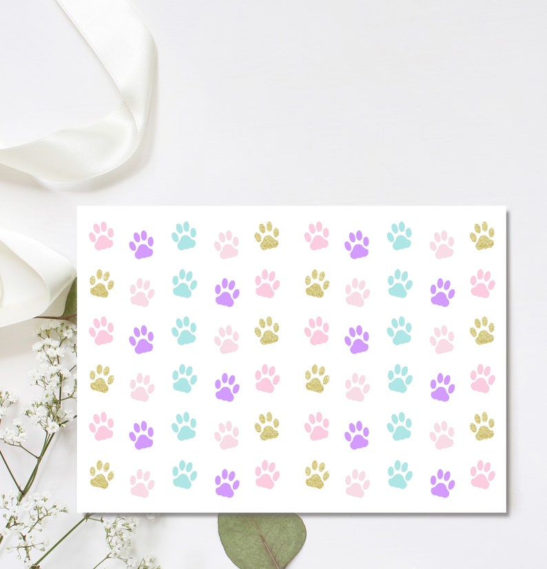 May include: A sheet of white paper with a repeating pattern of paw prints in pink, purple, turquoise, and gold glitter.