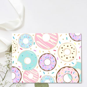 May include: A white background with a pattern of colorful donuts with sprinkles and frosting. The donuts are arranged in a random pattern and are surrounded by gold glitter.