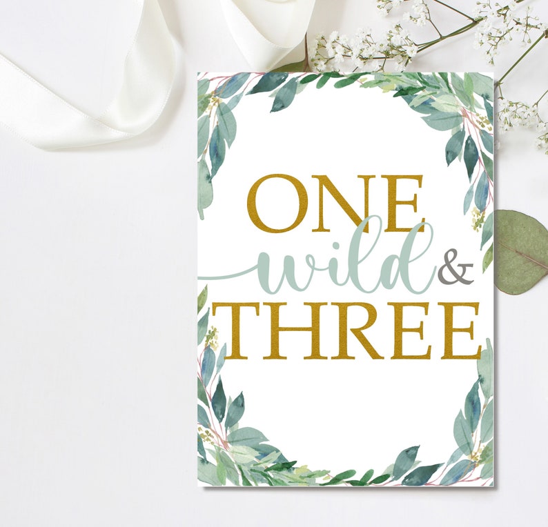 Peut inclure: Une affiche rectangulaire blanche avec l'inscription "ONE wild & THREE" en or et bleu clair. L'affiche est encadr&eacute;e d'une bordure de feuilles et de verdure aquarelles vertes et bleues.