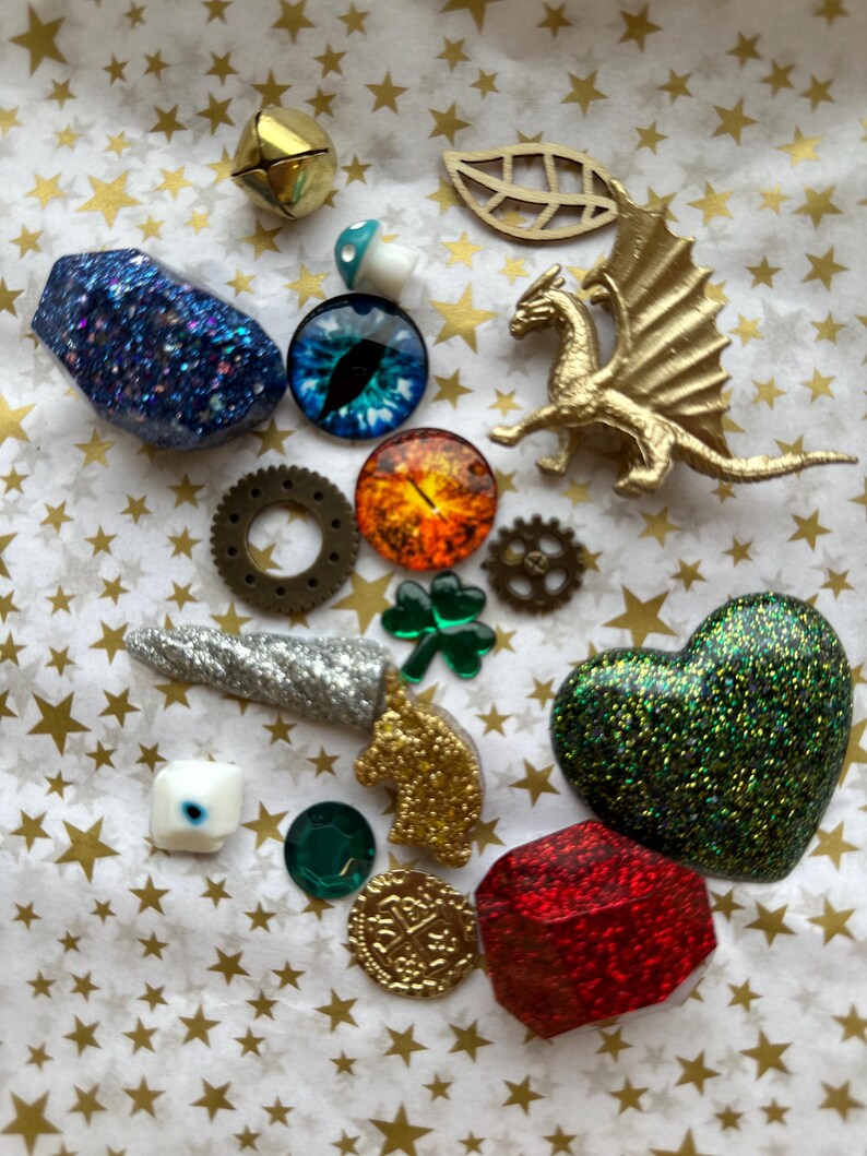 K&ouml;nnte beinhalten: Eine Sammlung dekorativer Verzierungen, darunter eine goldene Drachenfigur, ein gr&uuml;nes Glitzerherz und ein blauer Glitzerstein. Weitere Artikel sind Zahnr&auml;der, eine M&uuml;nze und ein vierbl&auml;ttriges Kleeblatt.