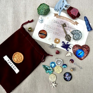 K&ouml;nnte beinhalten: Ein burgunderfarbener Samtbeutel mit einem goldenen Wachssiegel und einem Etikett mit der Aufschrift "vivian" neben verschiedenen Fantasy-Charms, Edelsteinen und einem Zertifikat. Das Zertifikat lautet "Official Dragon Knight Certificate".