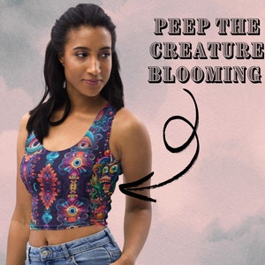 May include: A woman wearing a crop top with a colorful, psychedelic print featuring eyes, flowers, and a creature. The text "PEEP THE CREATURE BLOOMING" is written above her.