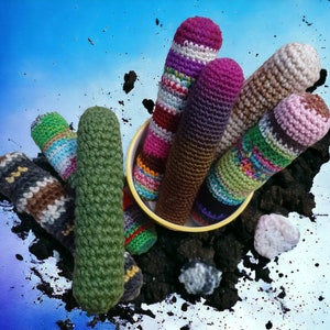 May include: A collection of colorful, handmade crochet cozies in various patterns and hues, including green, purple, and brown. Some are striped, others solid, and all are cylindrical in shape. They are arranged in a yellow bowl and scattered on a dark, earthy surface.