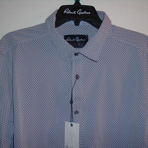 Puede incluir: Camisa azul claro con un peque&ntilde;o estampado de cuadros, colgada de una percha negra. El nombre de la marca "Robert Graham" est&aacute; impreso en la percha y una etiqueta. La camisa tiene cuello abotonado.