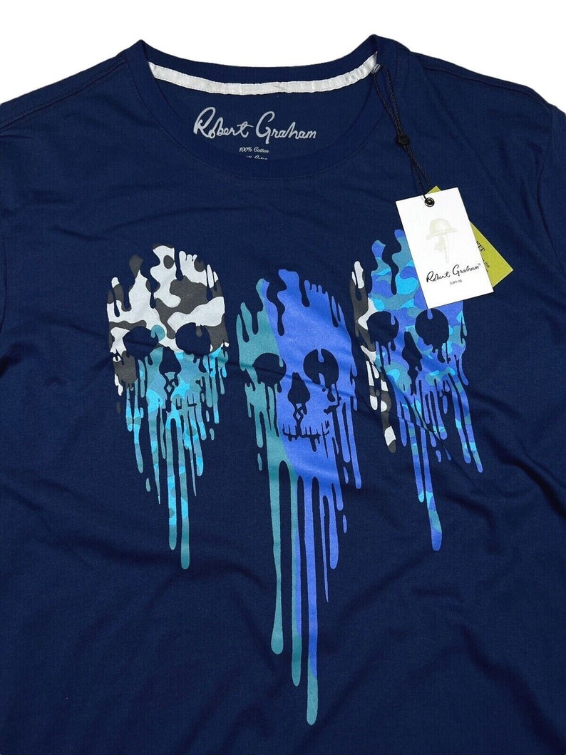 K&ouml;nnte beinhalten: Ein marineblaues T-Shirt mit einem grafischen Druck von drei tropfenden Sch&auml;deln in Blaut&ouml;nen und Gr&uuml;n. Die Sch&auml;del sind mit Tarnmustern gestaltet.