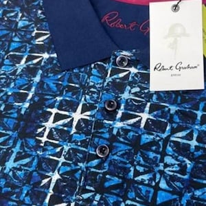 Op de afbeelding: Een blauw en wit gepatroneerd poloshirt met een donkerblauwe kraag en een roze binnenkraag. Het shirt heeft een knoopsluiting en een Robert Graham label.