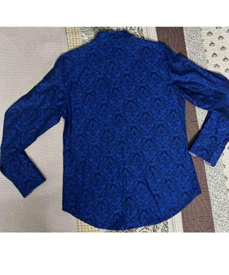 May include: A long-sleeved blue shirt with a dark blue floral pattern. The shirt is made of a soft material and has a classic design. The shirt is laid flat on a patterned surface.