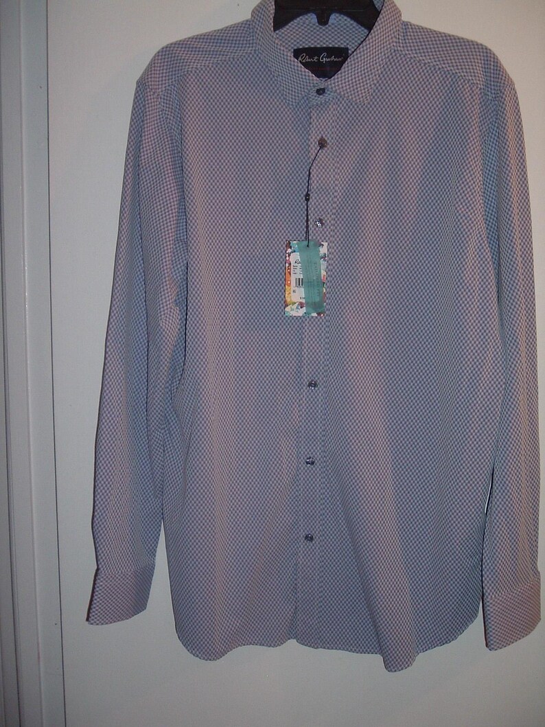 Puede incluir: Una camisa de manga larga con un peque&ntilde;o estampado de cuadros en tonos azules y blancos. La camisa tiene cuello y pu&ntilde;os cl&aacute;sicos, y una etiqueta adjunta cerca de los botones. La marca "Robert Graham" es visible en el cuello.