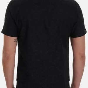 Puede incluir: Una camisa negra de manga corta con botones. La camisa tiene un cuello cl&aacute;sico y est&aacute; hecha de una tela oscura lisa. La vista trasera muestra el dise&ntilde;o y el ajuste de la camisa. El modelo lleva vaqueros azul oscuro.