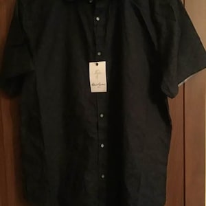 Puede incluir: Una camisa negra de manga corta con cuello y etiqueta. La camisa tiene una apariencia texturizada y una tela estampada en contraste en el interior del cuello y los pu&ntilde;os. La etiqueta dice "Robert Graham".