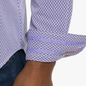 Puede incluir: Primer plano de una camisa de manga larga con un estampado de cuadros en morado claro y blanco. El pu&ntilde;o est&aacute; doblado, revelando un ribete liso en morado claro. La camisa se combina con vaqueros azules.